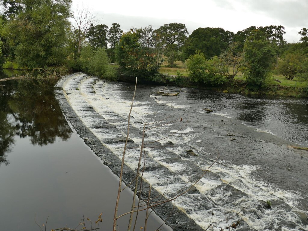 Greenholme weir on the River Wharfe, water pouring over a long stone weir with woodland behind